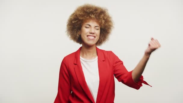 光の背景で成功と達成を象徴する フェイストポンプジェスチャーを作る赤いブレーザーのカーリーヘアを持つ楽しい女性 — ストック動画