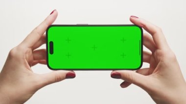 İki el yatay bir akıllı telefonu canlı yeşil ekranla tutuyor, içerik değişimine hazır.