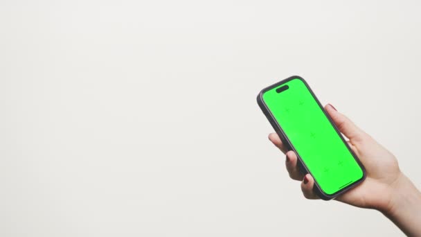 白い背景に隔離された緑色のスクリーンでスマートフォンを保持する手のクローズアップ — ストック動画