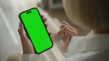 Manikürlü eli olan birinin tuttuğu yeşil ekranlı akıllı telefonun içerik değişimi için hazır hali.