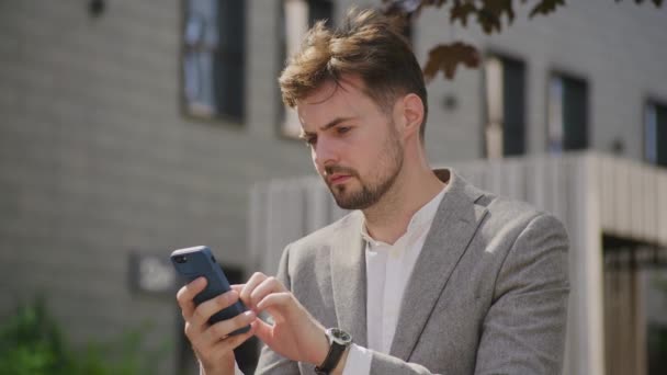 똑똑한 캐주얼 사업가가 밖에서 자신의 스마트 폰에서 무언가를 스러워 보인다 — 비디오