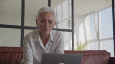 Gözlüklü kıdemli iş kadını modern bir ofis bilgisayarında işine konsantre oluyor.