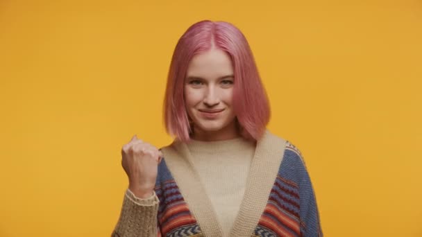 黄色の背景に強さや勝利のジェスチャーで拳を作るピンクの髪の自信のある若い少女 — ストック動画