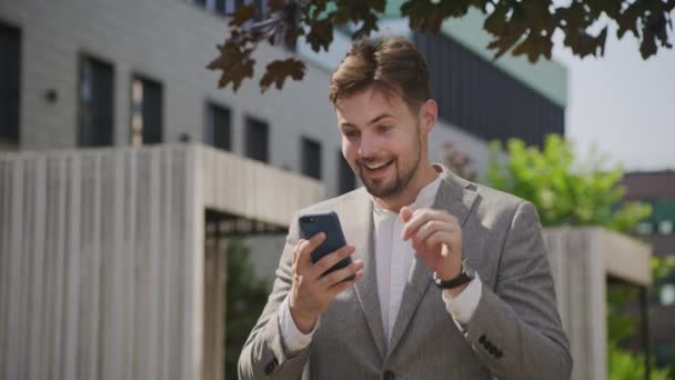 Fröhlicher Junger Mann Anzug Jubelt Während Auf Sein Telefon Blickt — Stockvideo