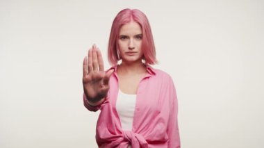 Pembe saçlı genç bir kadın dur işareti gösteriyor, beyaz bir arka planda sınırları işaret ediyor.