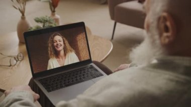 Rahat bir evde oturan yaşlı bir beyefendi bilgisayarında gülümseyen genç bir bayanla görüntülü sohbet ediyor.