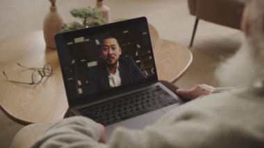 Üst düzey bir adam, bilgisayarında iyi giyimli bir işadamıyla evinden online bir toplantıya katılıyor.