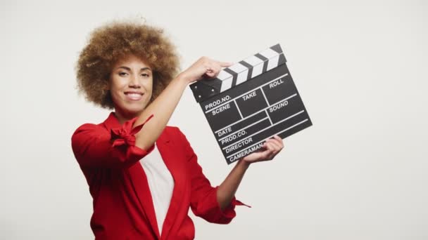 一个面带微笑的女人 有着充满活力的非洲式发型 手里拿着一个电影剪贴板 准备开始一个场景 — 图库视频影像