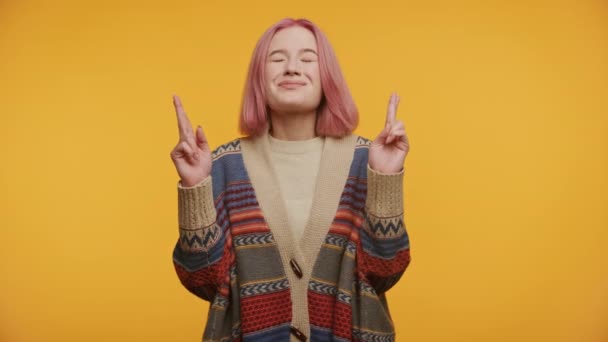 笑顔の若い女性 セーターでピンクの髪 目を閉じて 指が交差し 黄色の背景 — ストック動画