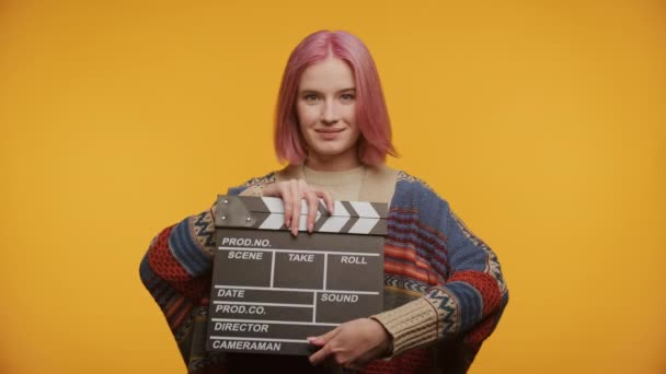 有自信的年轻女子 一头粉色的头发 拿着一块板子 准备拍电影 背景是黄色的 — 图库视频影像