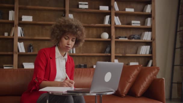 ロフトオフィスで彼女のラップトップで作業中にノートを取る赤のビジネスマン — ストック動画