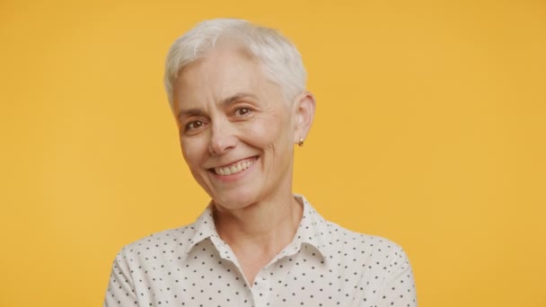 鮮やかな黄色の背景を持つポルカドットブラウスで微笑む陽気な高齢女性 — ストック動画