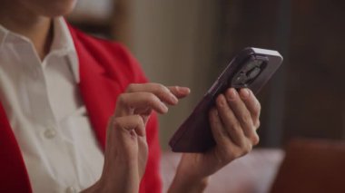 Kırmızı ceketli profesyonel bir kadın akıllı telefon kullanıyor, muhtemelen bir uygulamayı kullanıyor ya da bir toplantı ayarlıyor.