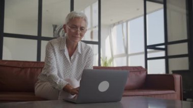 Evde dizüstü bilgisayarında zaferi kutlayan gözlüklü yaşlı bir kadın.