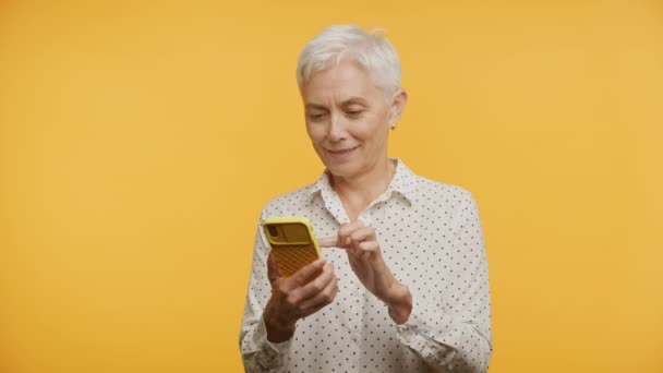 Χαμογελώντας Ηλικιωμένη Γυναίκα Χρησιμοποιώντας Ένα Smartphone Ένα Ζωντανό Κίτρινο Φόντο — Αρχείο Βίντεο