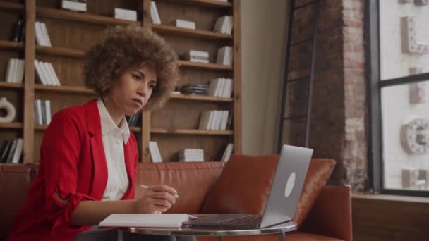 Pochłonięta Bizneswoman Afro Fryzura Robi Notatki Podczas Pracy Laptopie Biurze — Wideo stockowe