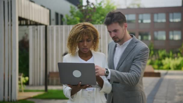 2人の専門家 灰色のブレーザーの男性 白いスーツの女性 都市の庭の設定で一緒にラップトップ上のコンテンツをレビュー — ストック動画