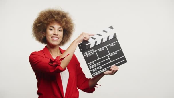 穿着红色衣服的快乐女人拿着电影剪贴板 背对着白色背景 — 图库视频影像