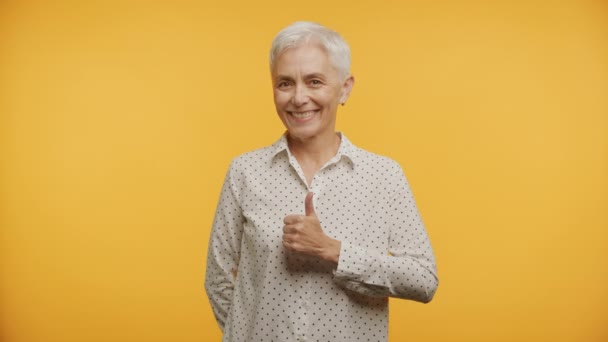 笑顔のシニア女性親指のジェスチャーを与える 黄色の背景にポルカドットブラウス — ストック動画