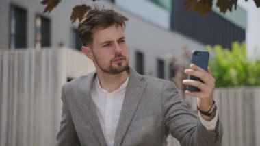 Gri takım elbiseli profesyonel bir adam iş görüşmesinde ya da açık hava konferansında akıllı telefon ekranına odaklanmış.