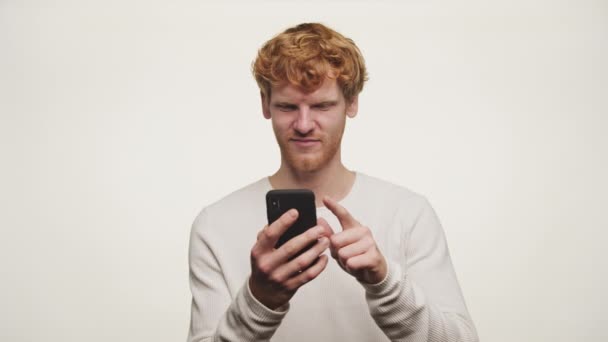 Wesoły Młody Człowiek Mruga Gestykuluje Znak Niepewności Trzymając Smartfona — Wideo stockowe