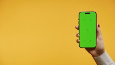 Bir el, yeşil ekranlı akıllı telefonu canlı sarı bir arka plana karşı krom tuşlamaya hazır bir şekilde tutar.