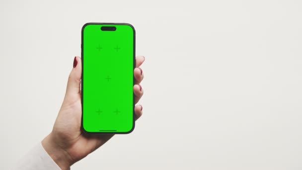ホワイトバックグラウンドのクロマキーグリーン画面でスマートフォンを保持する左手 — ストック動画