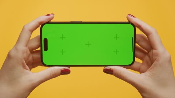 手持智能手机的手水平地与黄色背景的绿色屏幕相对照 — 图库视频影像