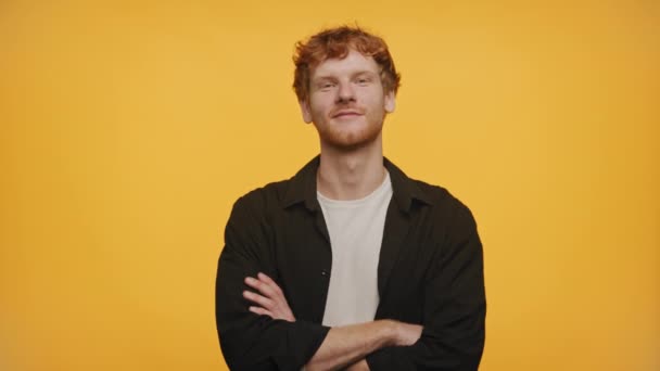 黄色の背景に自信を持って立っている赤い髪とカジュアルな服の笑顔の若い男性 — ストック動画
