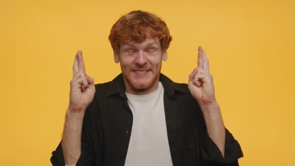 黄色の背景に隔離された 幸運のための指を閉じた目を持つ陽気な赤毛の男 — ストック動画