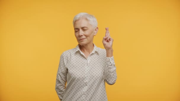 黄色い背景のための指を交差閉じた目を持つ楽観的な高齢女性 — ストック動画
