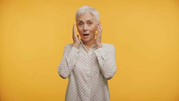 鮮やかな黄色の背景に対して 頬の手 ショックを受けた高齢女性 — ストック動画
