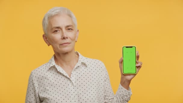 Ældre Kvinde Viser Mobiltelefon Med Chroma Nøgle Skærm Isoleret Gul – Stock-video