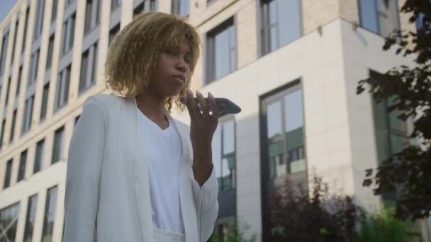 都市設定でモバイルボイスアシスタントに話すプロのアフリカ系アメリカ人女性 — ストック動画