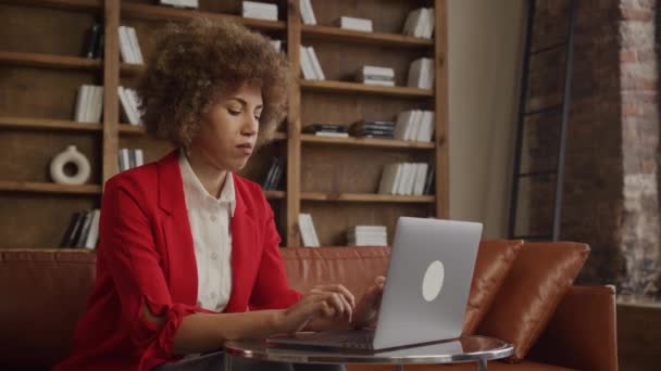 スタイリッシュなロフトオフィスで彼女のラップトップで熟考しながら赤いスーツで思慮深い実業家 — ストック動画