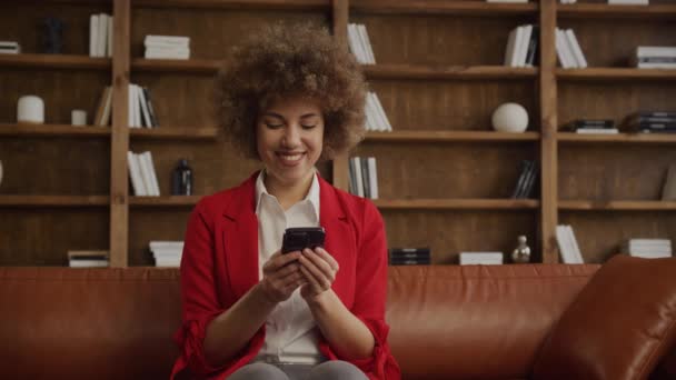 穿着红色夹克的快乐的非洲裔美国女人 用手机 舒适的办公环境 — 图库视频影像