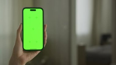 Uygulama sunumu ya da dijital düzenleme için hazır parlak yeşil ekranlı, bulanık oda arkaplanlı, dikey bir akıllı telefon.