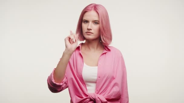 一个有着醒目的粉色头发的年轻女子的画像 用她的手在苍白的背景上做一个警告的手势 — 图库视频影像