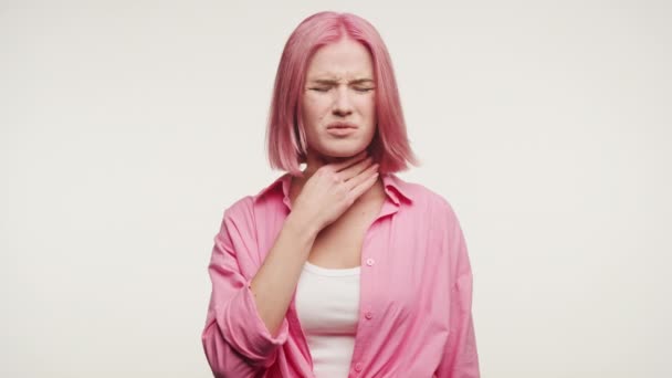 ピンクの髪の若い女性の撮影 彼女の喉に触れ 不快感や喉の痛みを示唆する顔を作る — ストック動画