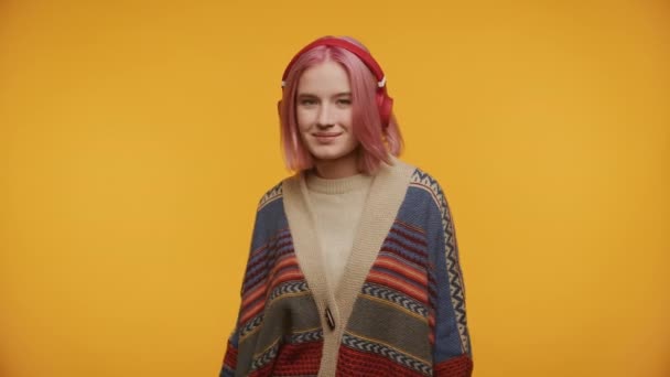 ピンクの髪の平和な若い女性 目を閉じて ヘッドフォンを着用し 活気に満ちた黄色の背景に対して居心地の良いセーター — ストック動画