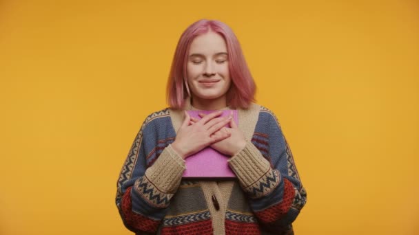 ピンクの髪の若い女性は 黄色い背景に彼女の心の近くに本を閉じている間 感謝して見上げます — ストック動画