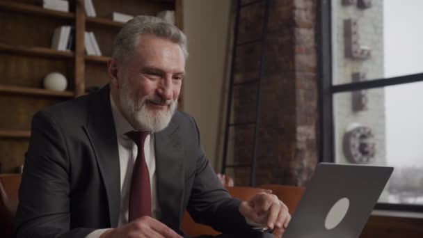 在现代阁楼的办公室里 一位快乐的资深商人一边看着笔记本电脑 一边庆祝一项成功的交易或成就 — 图库视频影像