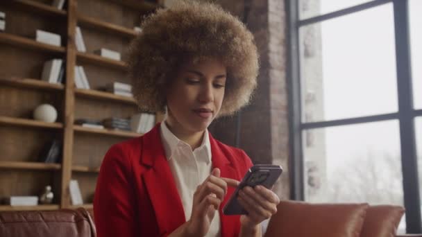 穿着红色夹克的快乐的女商人在一间有阁楼美感的办公室里用智能手机 — 图库视频影像