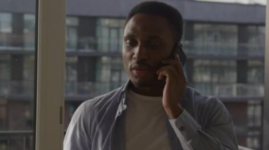 Odaklanmış bir adam pencere kenarında kentsel bir arkaplan ile bir telefon görüşmesi yapıyor.