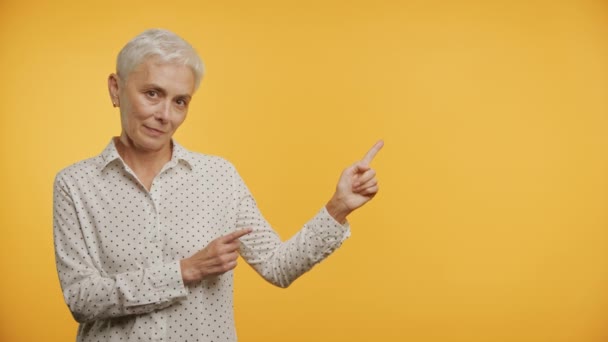 一位优雅的老年妇女的画像 她有一头短而白的头发 穿着一件波尔卡圆点衬衫 自信地指着她的侧面 面对着一个充满活力的黄色背景 — 图库视频影像