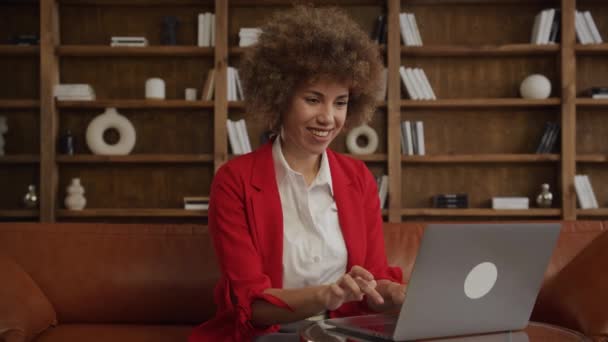 在现代的办公室里 身穿红色夹克的年轻女性满脸笑容 用笔记本电脑读着积极的信息 — 图库视频影像