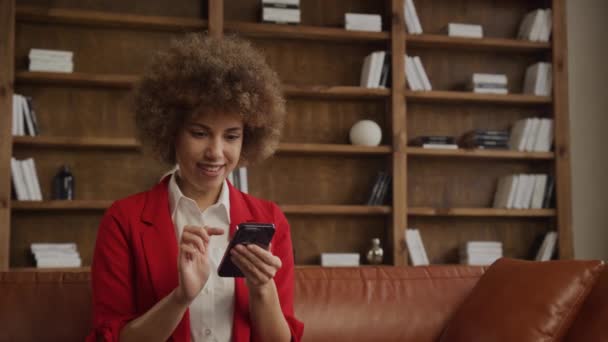 笑着穿红衫的年轻创业者开心地上网浏览她的智能手机 交流理念 — 图库视频影像