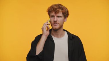 Kıvırcık saçlı genç adam, tek renkli sarı bir arka plana kurulmuş sarı bir akıllı telefondan derin bir sohbete daldı.