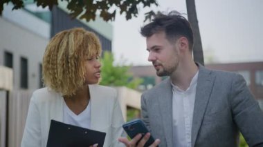 Profesyonel bir erkek ve kadın iş ile ilgili konuları tartışırken dışarıdaki bir akıllı telefondan bilgileri gözden geçirirler.