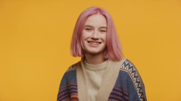 笑容可亲的年轻姑娘 戴着大括号 一头粉红的头发 手舞足蹈 在鲜亮的黄色背景下舞动 — 图库视频影像